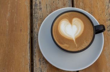 A cup of coffee with heart pattern in a black cup on wooden background