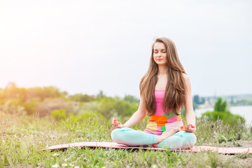 Pretty woman doing yoga exercises on nature landscape