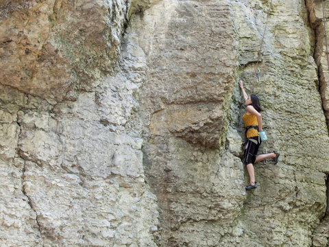 Young woman with rope climbs on the rock.