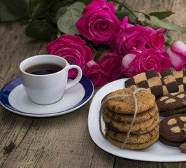 cup of coffee and cookies on a plate with a bouquet of roses