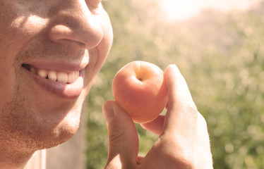 Cheerful guy eating apricots at the garden 
