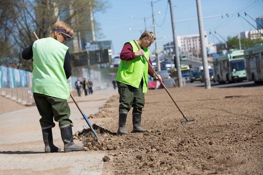 City landscapers preparing soil along street for grass planting with rake tools