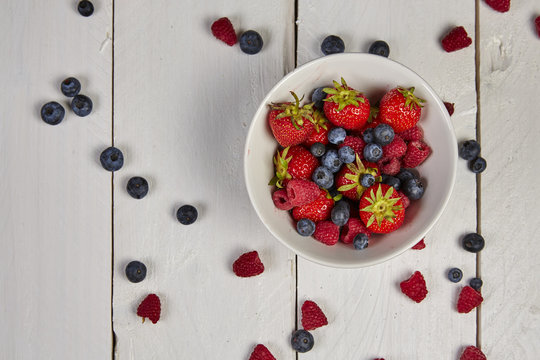 Different berries in a white bowl on a white wooden