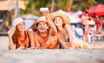 Group of happy young people lying on wite beach sand and taking