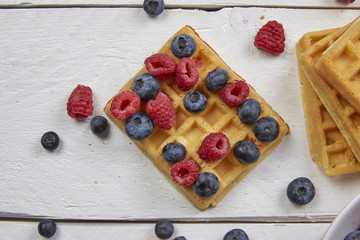 Naklejka na ściany i meble Different berries on a waffle and in a bowl on a white wooden table