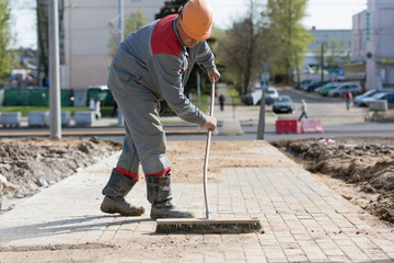 Construction worker grouting dry sand with brush into paver joints