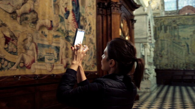 Woman taking photo of fresco with cellphone in church
