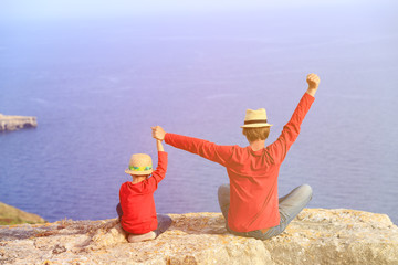 happy father and son sitting on top of a mountain