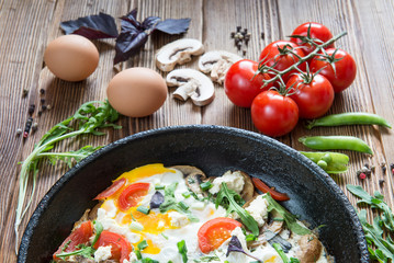 Fried eggs on pan with vegetabls on rustic wooden background