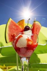 Eisbecher mit verschiedenen Früchten, Sonne, blauer Himmel, Sonnenschirme