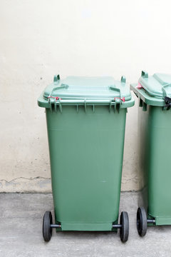 Green plastic garbage bin on white wall in factory