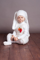 Obraz premium Smiling baby boy 3-4 year old sitting on wooden floor in room. Childhood. Wearing hare costume.