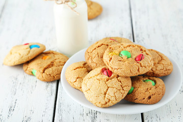 Cookies with colorful candy in plate on white wooden background