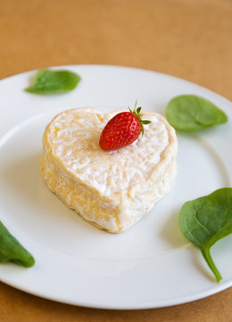Сыр сердце с клубникой и салатом на белой тарелке сверху