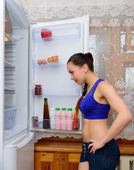 The girl looks curiously into the open refrigerator