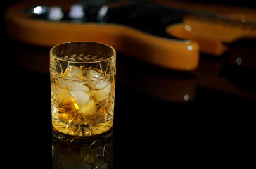 A glass of whiskey on the rocks and old guitar.