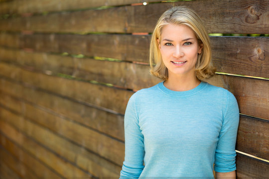 Beautiful blonde woman portrait smiles next to wood fence