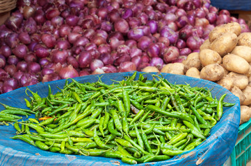Pile of fresh green chili peppers, onions, potatoes on the market