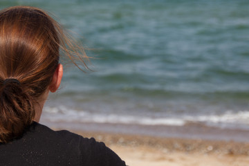 Frau sitzt am Strand und Blickt aufs Meer