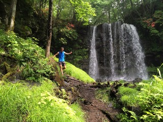 Fototapeta premium Runner on forest trail with waterfall behind