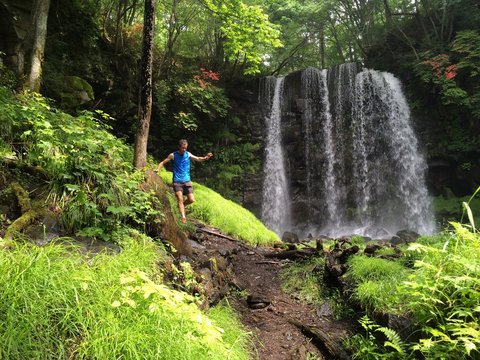 Runner on forest trail with waterfall behind