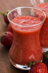 A glass of strawberry smoothie on a wooden background