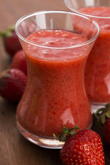 A glass of strawberry smoothie on a wooden background