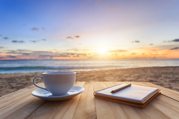 Obraz premium Coffee cup on wood table at sunset or sunrise beach