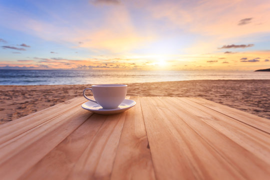 Fototapeta Coffee cup on wood table at sunset or sunrise beach