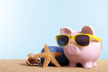 Piggy Bank or piggybank wearing sunglasses standing on a sunny tropical beach with towel holiday...