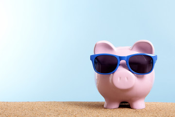 Piggy Bank or piggybank wearing sunglasses standing on a sunny tropical beach with holiday vacation...
