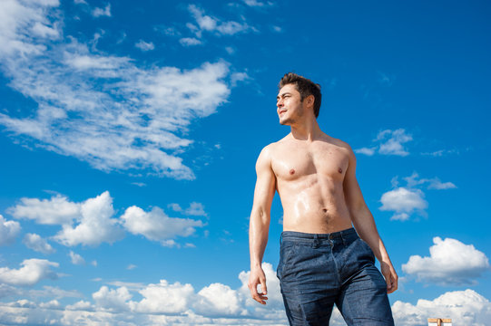 Fit young man with bare torso standing under scenic blue sky on sunny day