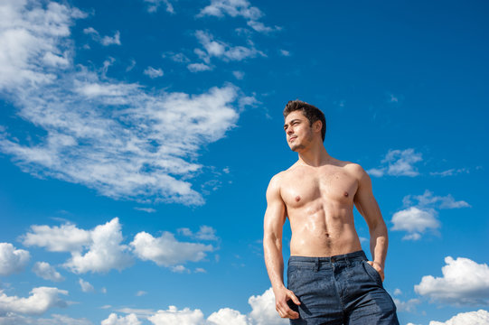 Fit young man with bare torso standing under scenic blue sky on sunny day