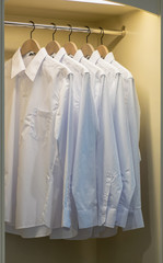 row of white shirts hanging on coat hanger in wardrobe