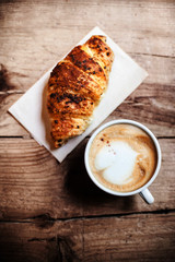 Coffee and fresh croissant for breakfast on rustic wooden table,