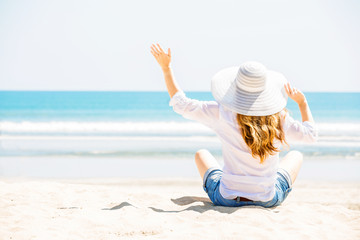 Beautifil young woman sitting on the beach at sunny day enjoing
