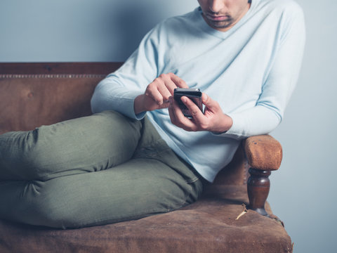 Young man sitting on sofa and using smart phone