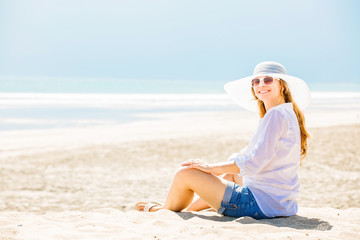 Fototapeta na wymiar Beautifil young woman sitting on the beach at sunny day enjoing