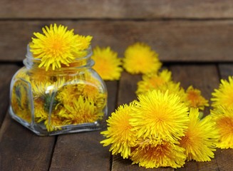 Flower honey in a glass jar and dandelions on a wooden table