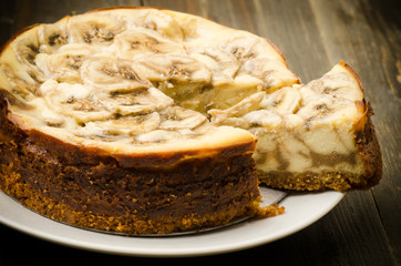 Homemade banana caramel cheesecake on wooden background