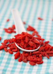 Dried goji berries in white spoon on checked fabric