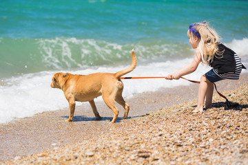 Pretty little girl with blond hair walking on the beach with a dog