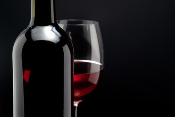 Red wine glass and a bottle in black background