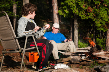 father and son sitting by a campfire roasting marshmallows