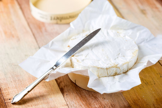 Camembert cheese wrapped in paper with vintage knife on wooden t