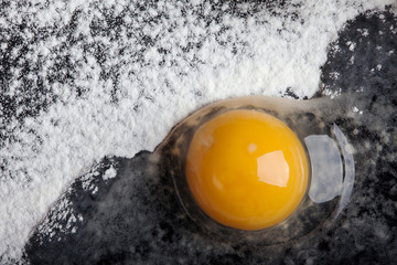 broken egg on  layer of flour on the black background