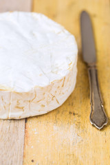 Camembert cheese wrapped in paper with vintage knife on wooden table