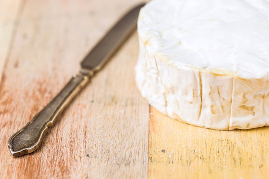 Camembert cheese wrapped in paper with vintage knife on wooden table
