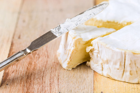 Camembert cheese with cut wedge and vintage knife on wooden tabl