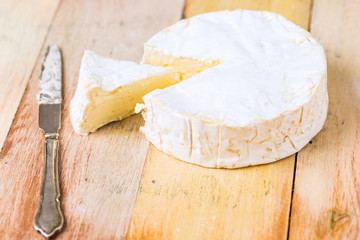 Camembert cheese wrapped in paper with vintage knife on wooden table
